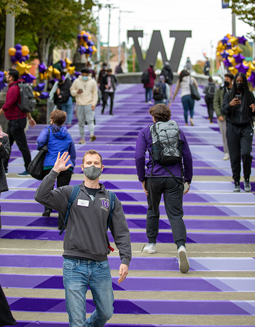 Student on grand stair case waving with other students around