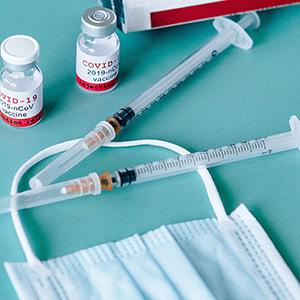 Illustration showing hypodermic needles, vaccine vials and a face covering