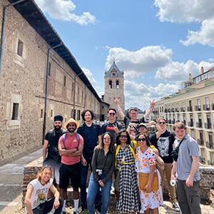 A group of UW Tacoma students stand outside the UW's León Center in Spain. There are tall, brick gothic buildings in the background.