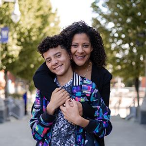 UW Tacoma alumna Alishia Agee-Cooper poses with her son on the Grand Staircase. She has her arms over her shoulder. They are smiling and holding hands.